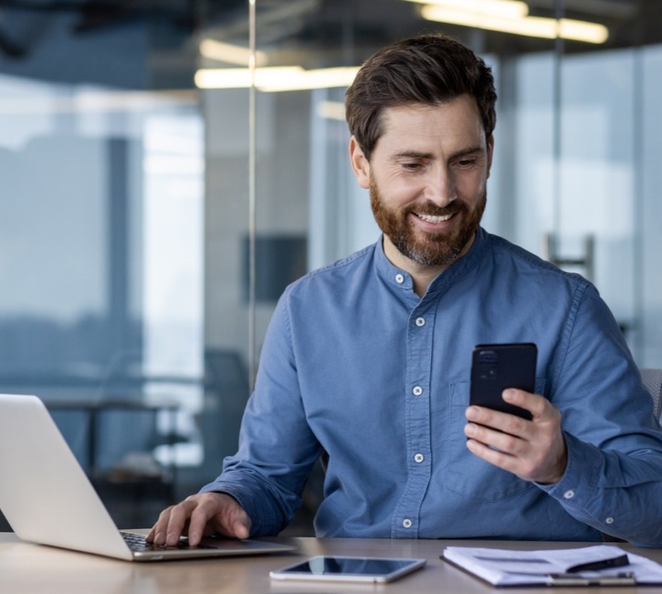 Man in blue at desk looking at phone_2461602205_edited